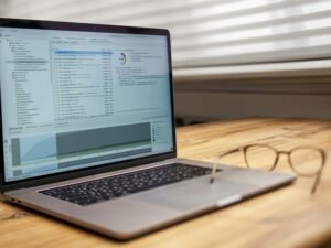 Offener Laptop und eine Brille liegen auf einem Holzschreibtisch, bereit für die Arbeit am Computer im Büro oder Homeoffice.