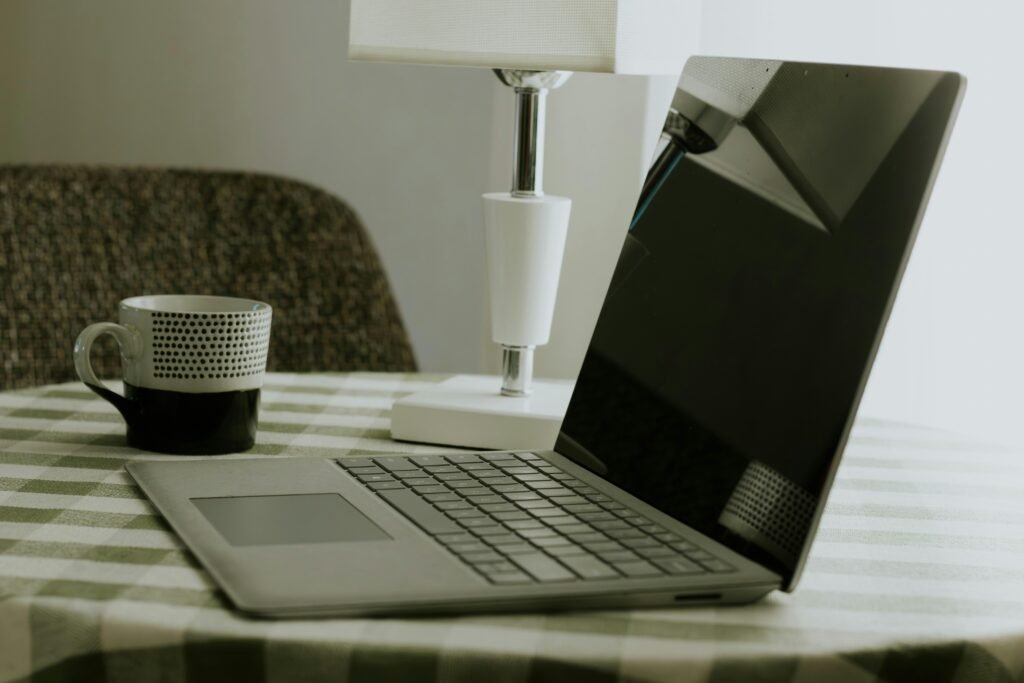 Laptop und weiße Kaffeetasse stehen auf einem schwarz-weiß karierten Tischtuch, ideale Szene für Homeoffice oder kreatives Arbeiten.