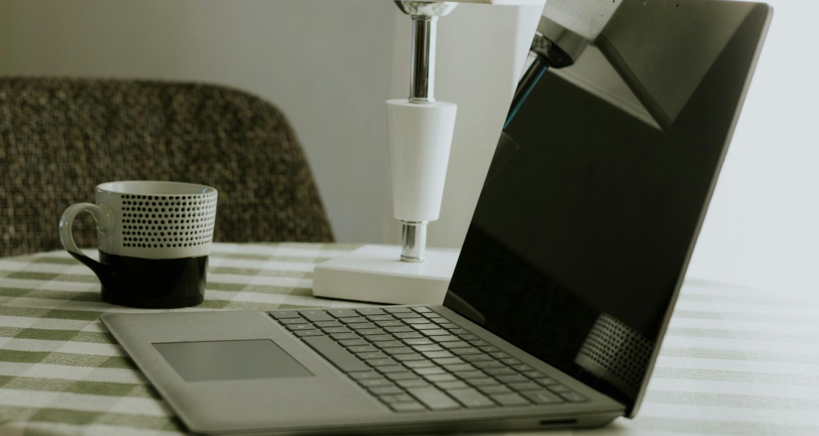 Laptop und weiße Kaffeetasse stehen auf einem schwarz-weiß karierten Tischtuch, ideale Szene für Homeoffice oder kreatives Arbeiten.