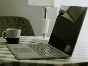 Laptop und weiße Kaffeetasse stehen auf einem schwarz-weiß karierten Tischtuch, ideale Szene für Homeoffice oder kreatives Arbeiten.