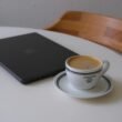 Laptop und Kaffeetasse stehen nebeneinander auf einem weißen Tisch, ideal für Homeoffice oder produktives Arbeiten.