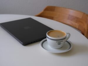 Laptop und Kaffeetasse stehen nebeneinander auf einem weißen Tisch, ideal für Homeoffice oder produktives Arbeiten.