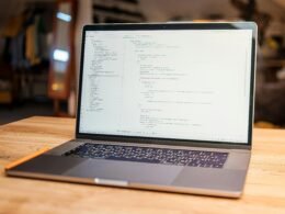 Laptop auf einem Tisch, auf dessen Bildschirm mehrere Zeilen Programmiercode angezeigt werden