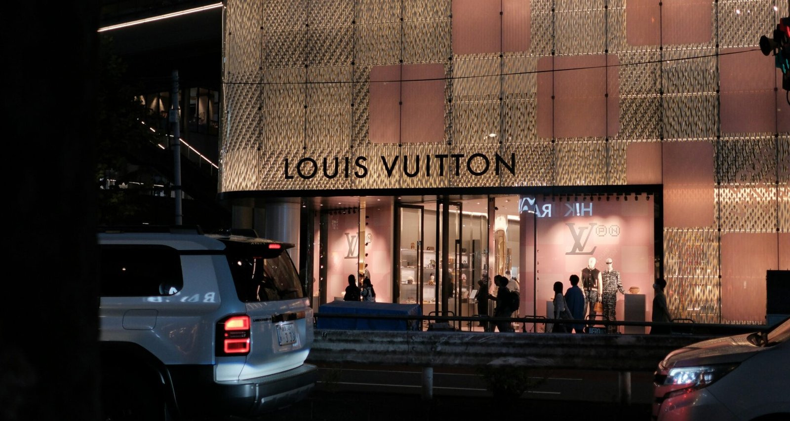 Louis Vuitton Geschäft bei Nacht, beleuchtete Fassade und Autos auf der Straße im urbanen Stadtbild