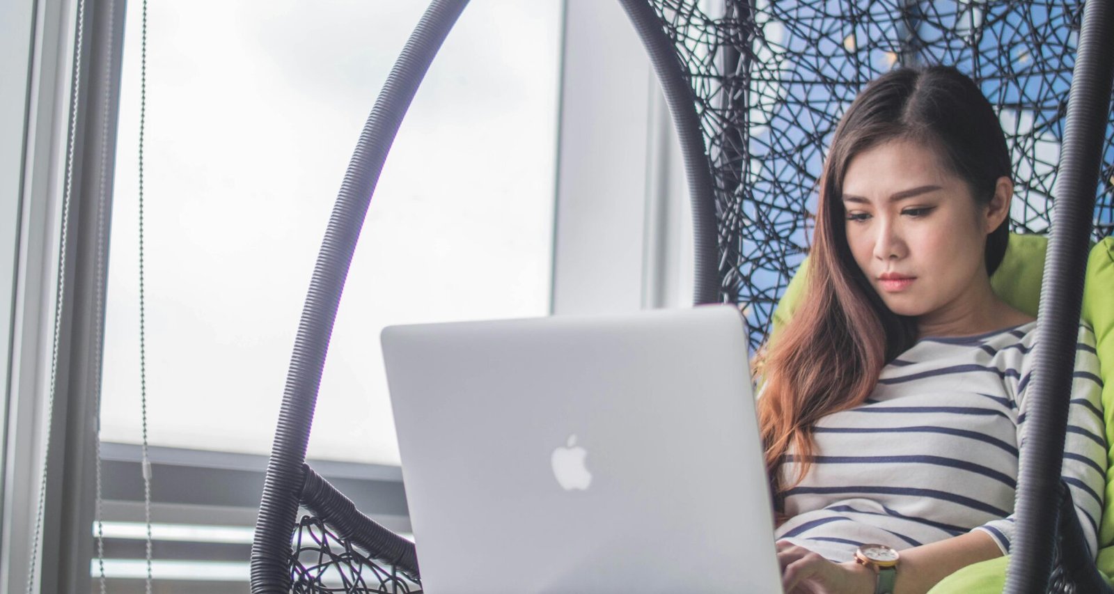 MacBook liegt auf dem Schoß einer Frau, die entspannt arbeitet – Symbolbild für mobiles Arbeiten von überall