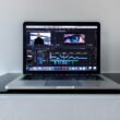 Ein MacBook Pro auf einem schwarzen Schreibtisch mit minimalistischem Setup, ideal für kreatives Arbeiten oder Online-Marketing Aufgaben.