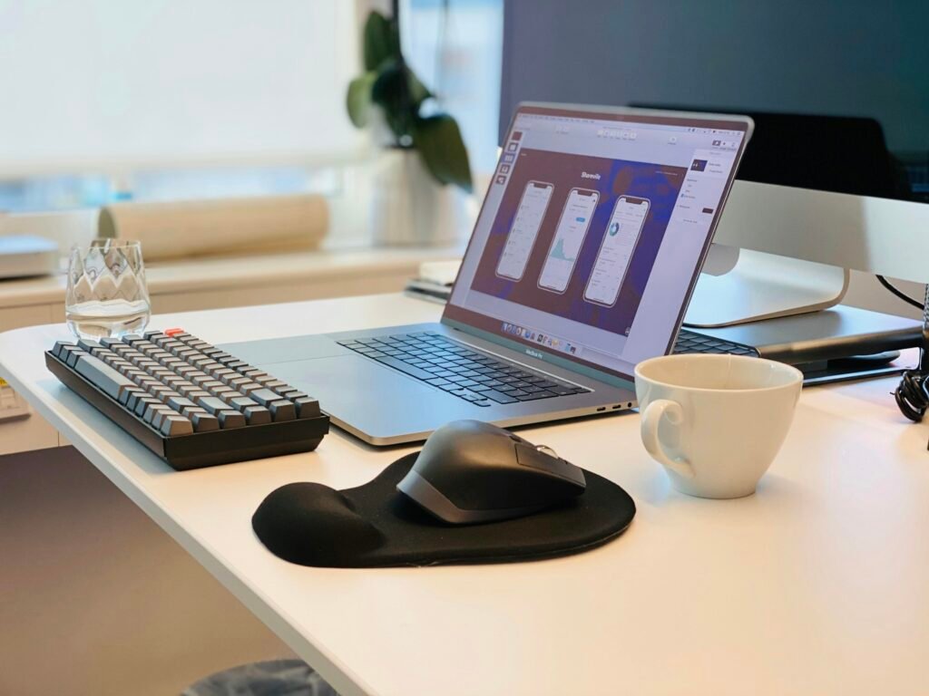 MacBook Pro neben schwarzer Computermaus und schwarzer Tastatur auf weißem Tisch, minimalistisch arrangiert