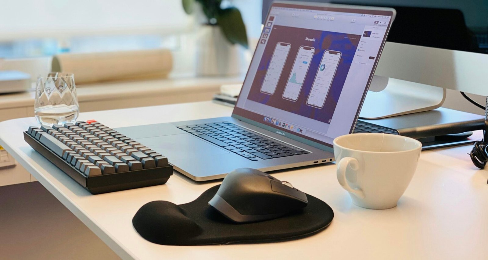 MacBook Pro neben schwarzer Computermaus und schwarzer Tastatur auf weißem Tisch, minimalistisch arrangiert