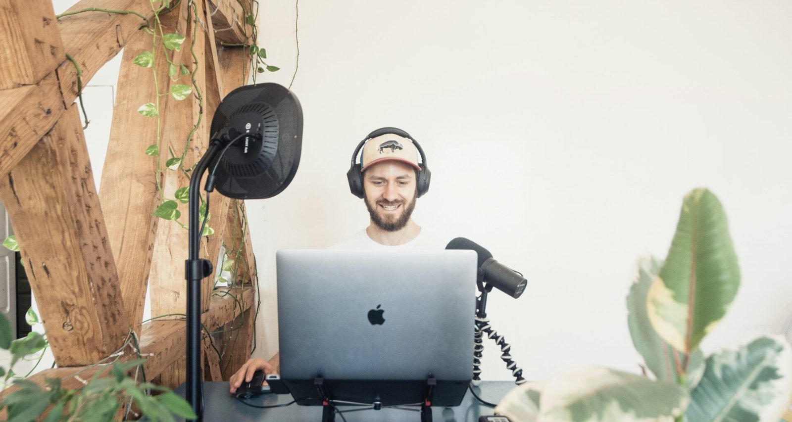 Mann mit schwarzen Kopfhörern sitzt am Tisch und benutzt ein MacBook Laptop in moderner Umgebung.