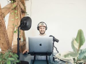 Mann mit schwarzen Kopfhörern sitzt am Tisch und benutzt ein MacBook Laptop in moderner Umgebung.