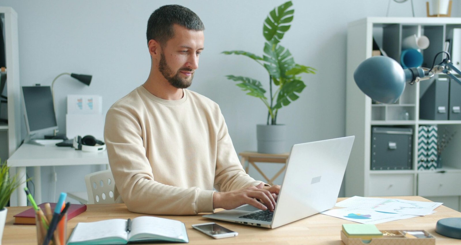 Mann arbeitet an einem Laptop an einem Schreibtisch mit Fokus auf Arbeitsumgebung und technische Ausstattung.