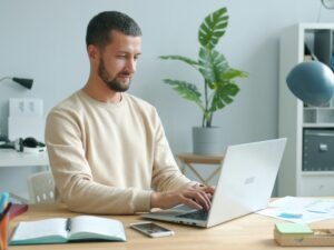 Mann arbeitet an einem Laptop an einem Schreibtisch mit Fokus auf Arbeitsumgebung und technische Ausstattung.