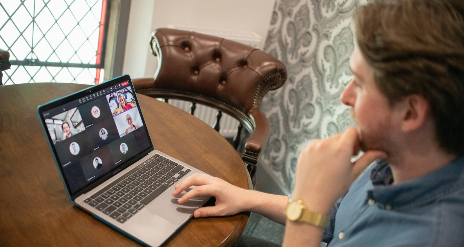 Ein Mann sitzt an einem Laptop und beteiligt sich an einer Videokonferenz in einer modernen Arbeitsumgebung.