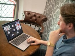 Ein Mann sitzt an einem Schreibtisch und nimmt mit seinem Laptop an einer Video-Konferenz teil