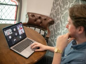 Ein Mann sitzt an einem Schreibtisch und nimmt mit seinem Laptop an einer Video-Konferenz teil