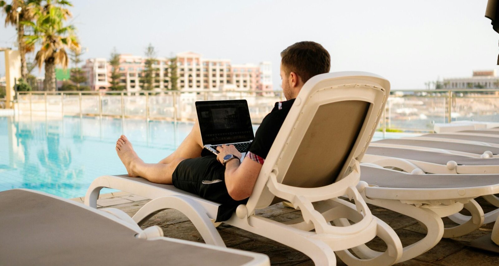 Mann liegt auf einer Sonnenliege und arbeitet mit einem Laptop, zeigt mobiles Arbeiten an einem sonnigen Ort