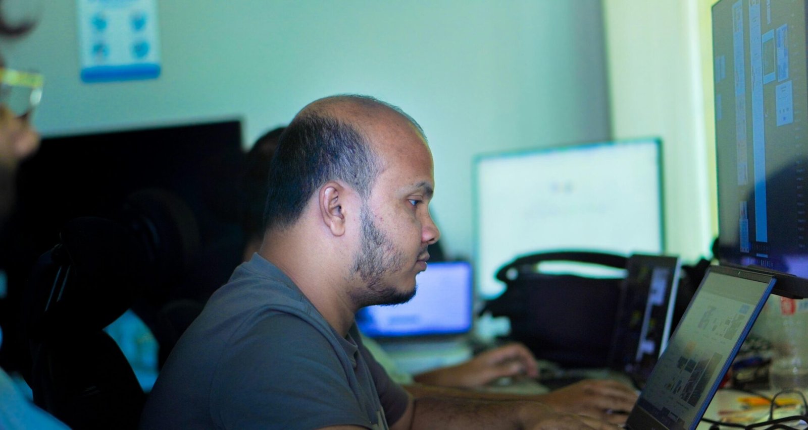 Mann arbeitet an einem Laptop an einem Schreibtisch in heller Büroatmosphäre mit modernen Arbeitsmitteln.