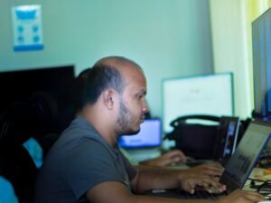 Mann arbeitet an einem Laptop an einem Schreibtisch in heller Büroatmosphäre mit modernen Arbeitsmitteln.