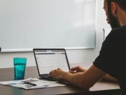 Ein Mann sitzt an einem Tisch und arbeitet an einem Laptop – ideale Darstellung für digitale Arbeitsumgebungen.