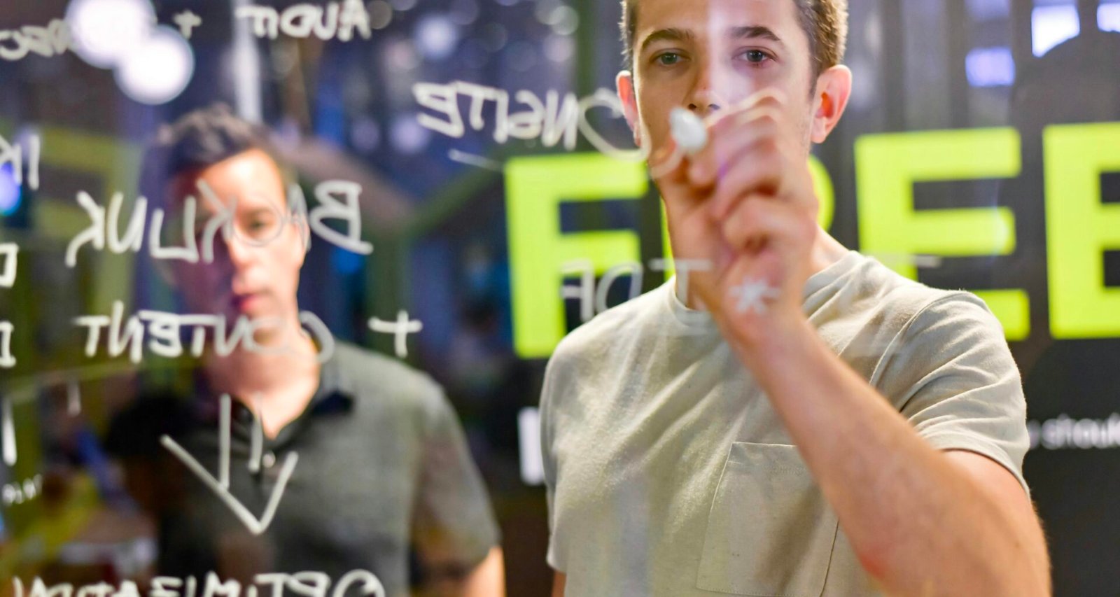 Mann schreibt mit Marker auf eine transparente Glaswand und plant Strategien oder Konzepte in einem modernen Büro