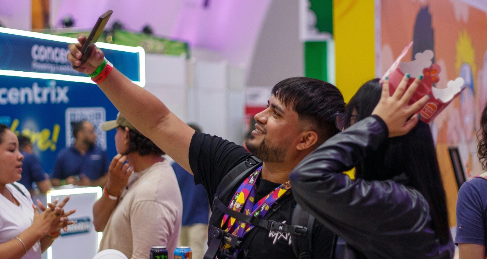 Mann mit Maske nimmt ein Selfie bei einer Veranstaltung auf, im Hintergrund sind weitere Teilnehmer sichtbar