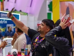 Ein Mann trägt eine Gesichtsmaske und macht auf einer Veranstaltung ein Selfie mit seinem Smartphone.