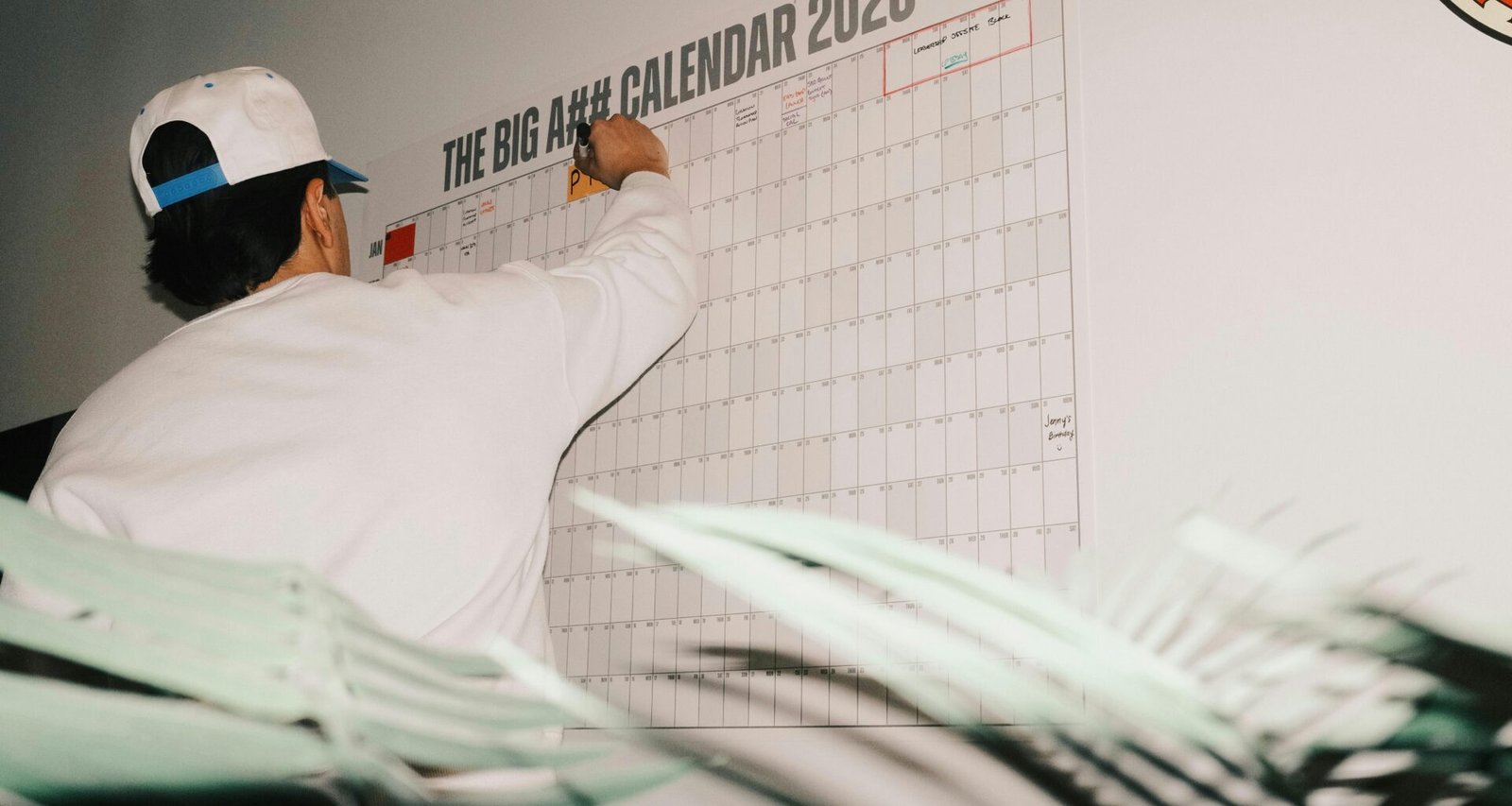 Ein Mann trägt Termine in einen großen Kalender für 2026 ein. Symbolbild für Planung und Zeitmanagement im digitalen Alltag.