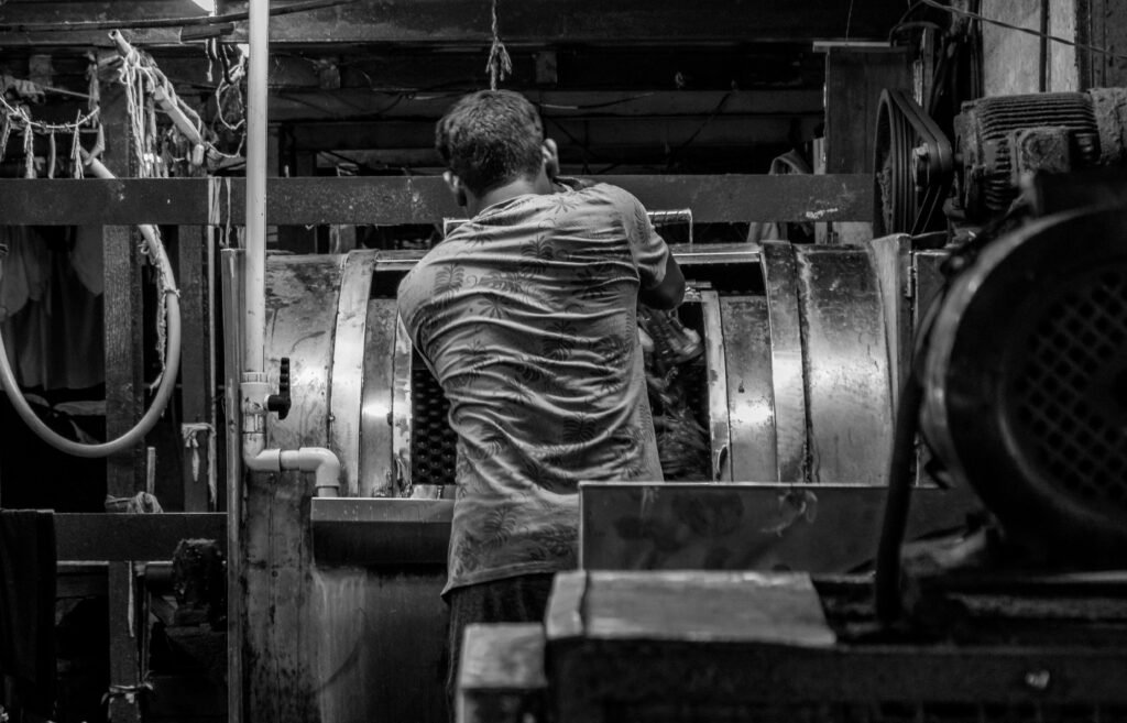 Ein Mann arbeitet in einer dunklen, industriellen Fabrikhalle mit stahlgrauer Ausstattung und Maschinen im Hintergrund.