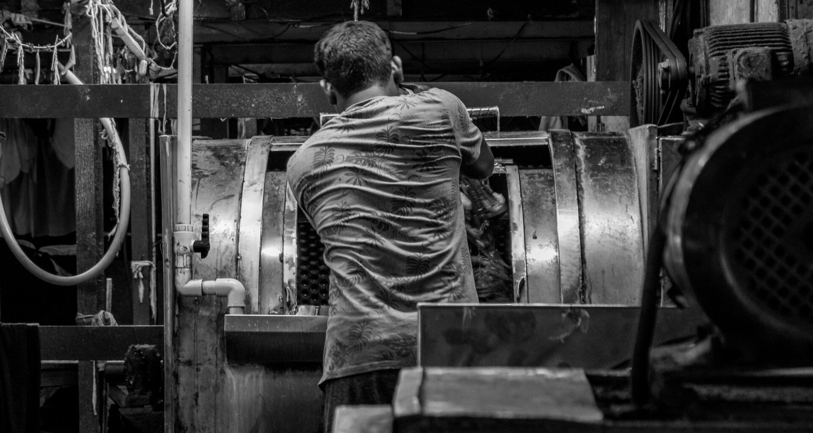 Ein Mann arbeitet in einer dunklen, industriellen Fabrikhalle mit stahlgrauer Ausstattung und Maschinen im Hintergrund.