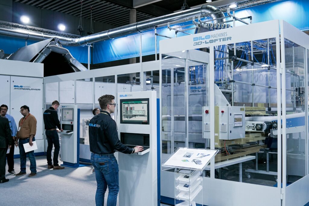 Mehrere Männer in einem modernen Büro, einer arbeitet am Computer, während sich andere Kollegen im Hintergrund unterhalten.