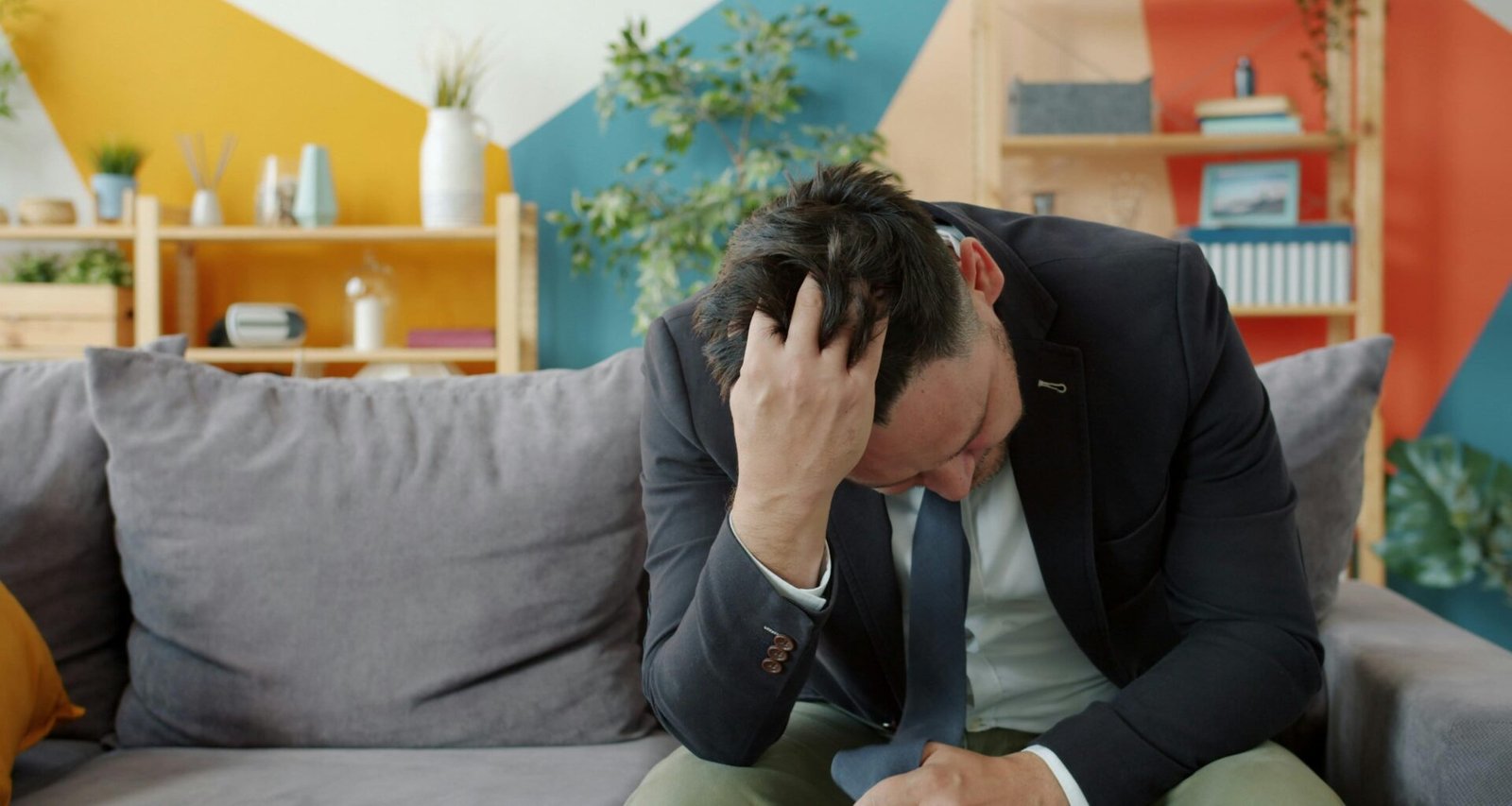 Mann im Anzug sitzt auf einem Sofa und stützt den Kopf in die Hände, fotografiert im Innenraum