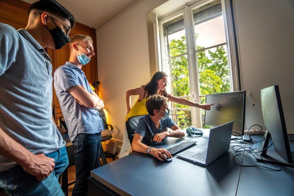 Zwei Männer stehen nebeneinander, einer im blauen Hemd, einer im gelben Polohemd, und unterhalten sich in einem Innenraum.