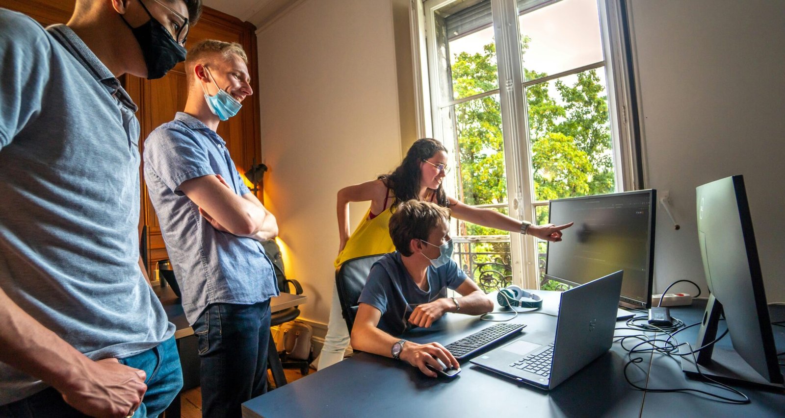 Zwei Männer stehen nebeneinander, einer im blauen Hemd, einer im gelben Polohemd, und unterhalten sich in einem Innenraum.