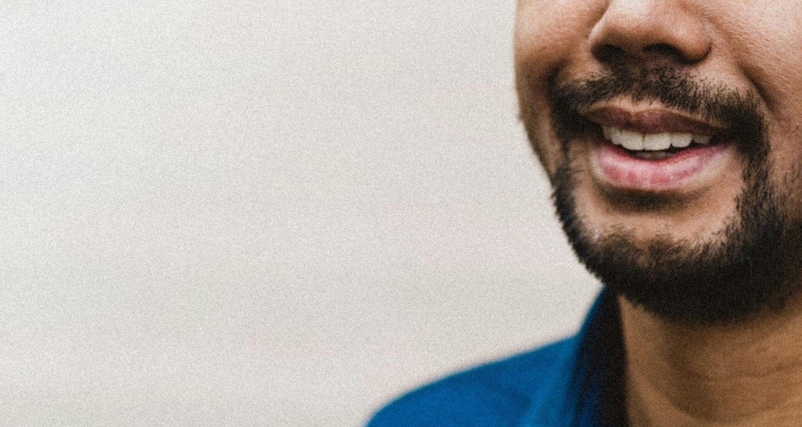 Ein Mann in einem blauen Polohemd steht vor neutralem Hintergrund und blickt freundlich in die Kamera.