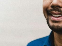 Ein Mann in einem blauen Polohemd steht vor neutralem Hintergrund und blickt freundlich in die Kamera.