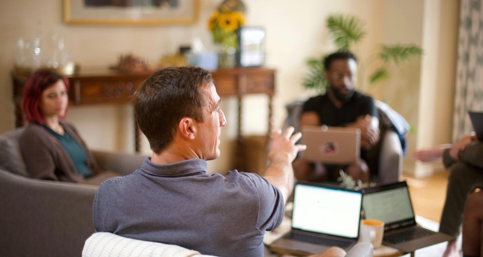 Ein Mann im grauen Pullover sitzt entspannt auf einem Sofa im modernen Wohnraum und arbeitet konzentriert am Laptop.