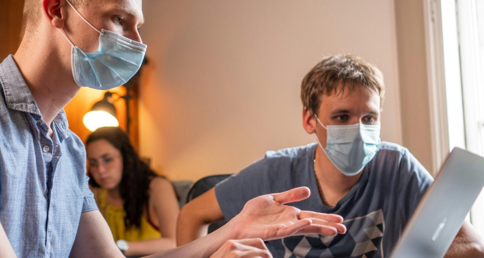 Mann mit grauem T-Shirt und weißer Gesichtsmaske steht vor neutralem Hintergrund, Schutzmaßnahme im Alltag