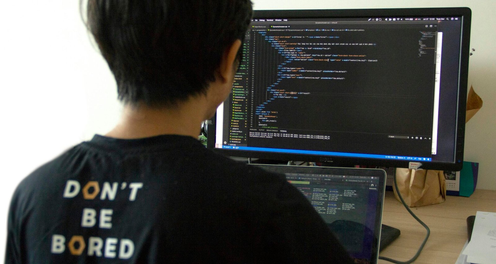 Mann mit schwarzem Shirt arbeitet am Laptop und Flachbildmonitor an einem modernen Arbeitsplatz