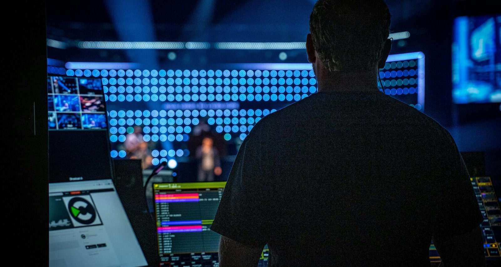 Ein Mann mit schwarzem Shirt bedient ein großes Audio-Mischpult in einem modernen Studio.