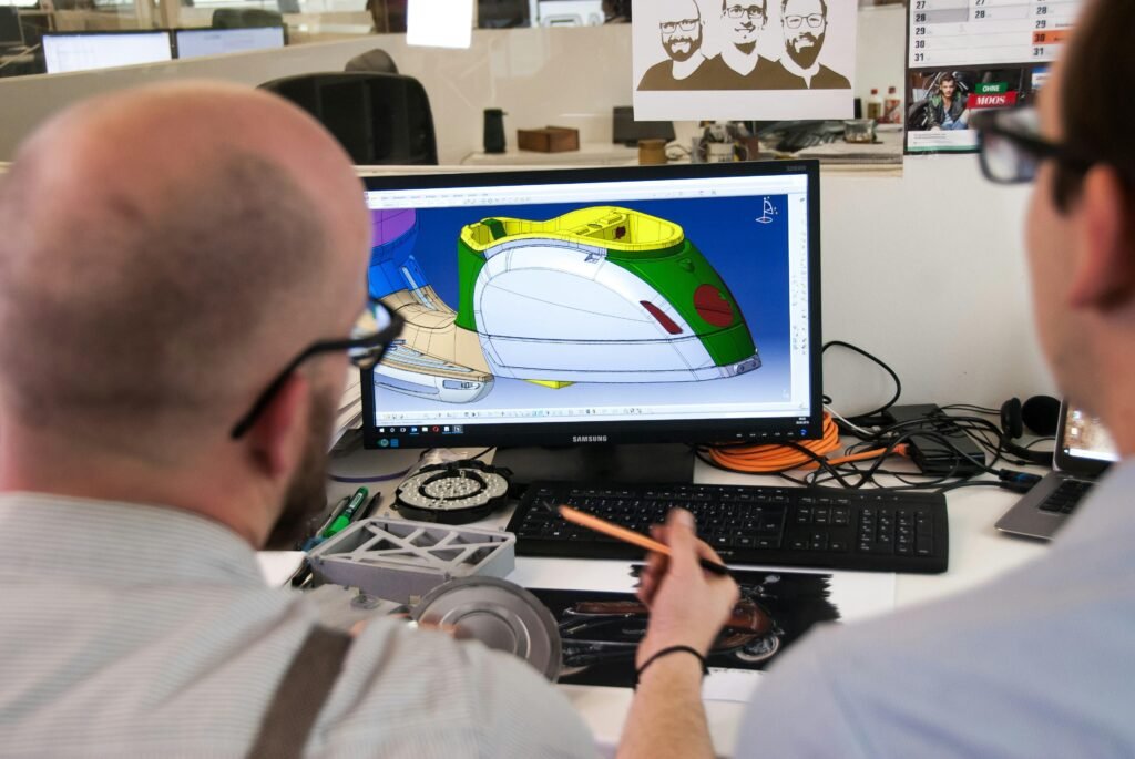 Ein Mann trägt ein weißes Hemd und schwarze Brille. Er sitzt an einem Schreibtisch bei der Arbeit in modernem Umfeld.