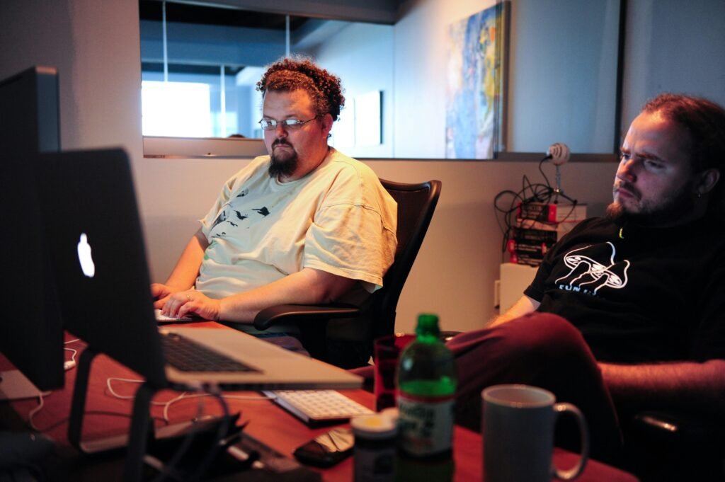 Ein Mann im weißen Crew Neck T-Shirt sitzt auf einem braunen Stuhl vor neutralem Hintergrund, Innenaufnahme