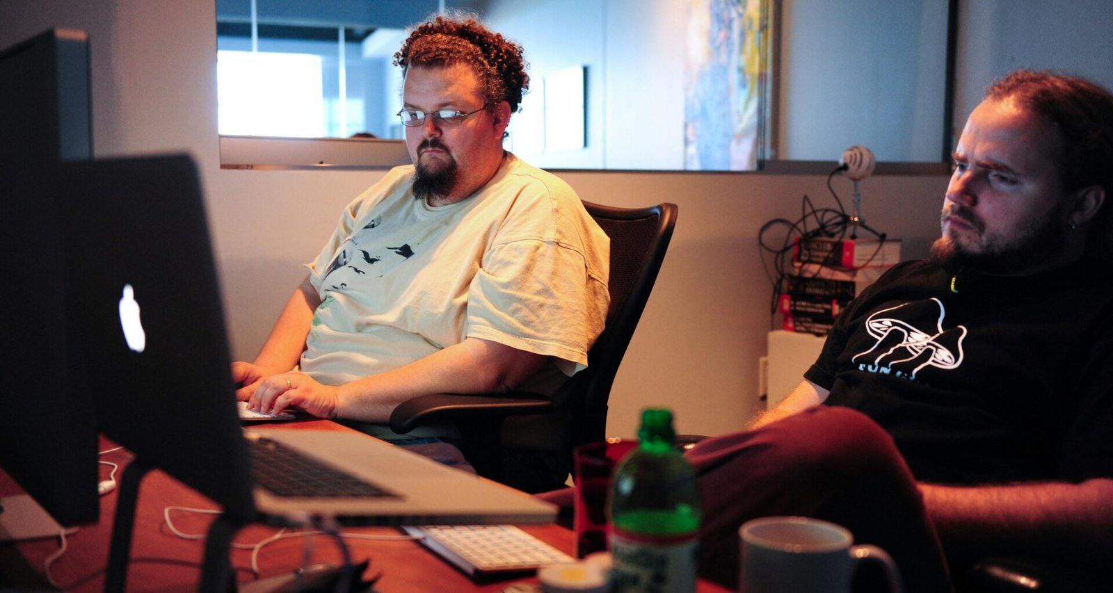 Ein Mann im weißen Crew Neck T-Shirt sitzt auf einem braunen Stuhl vor neutralem Hintergrund, Innenaufnahme