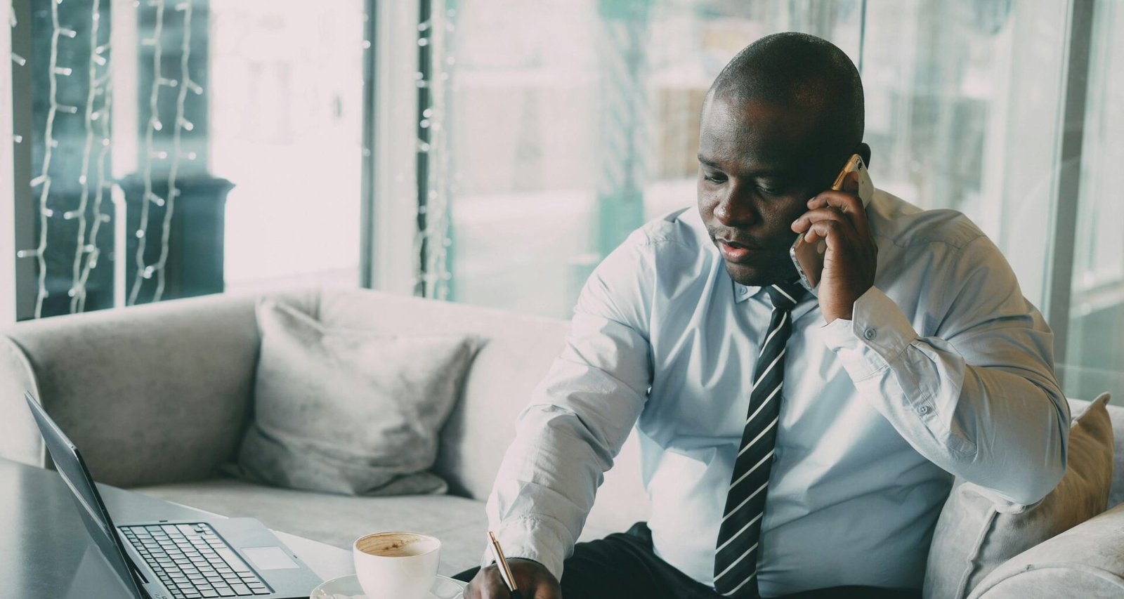 Mann im Büroumfeld mit Hemd und Krawatte, telefonierend am Schreibtisch sitzend, moderner Arbeitsplatz mit Unterlagen