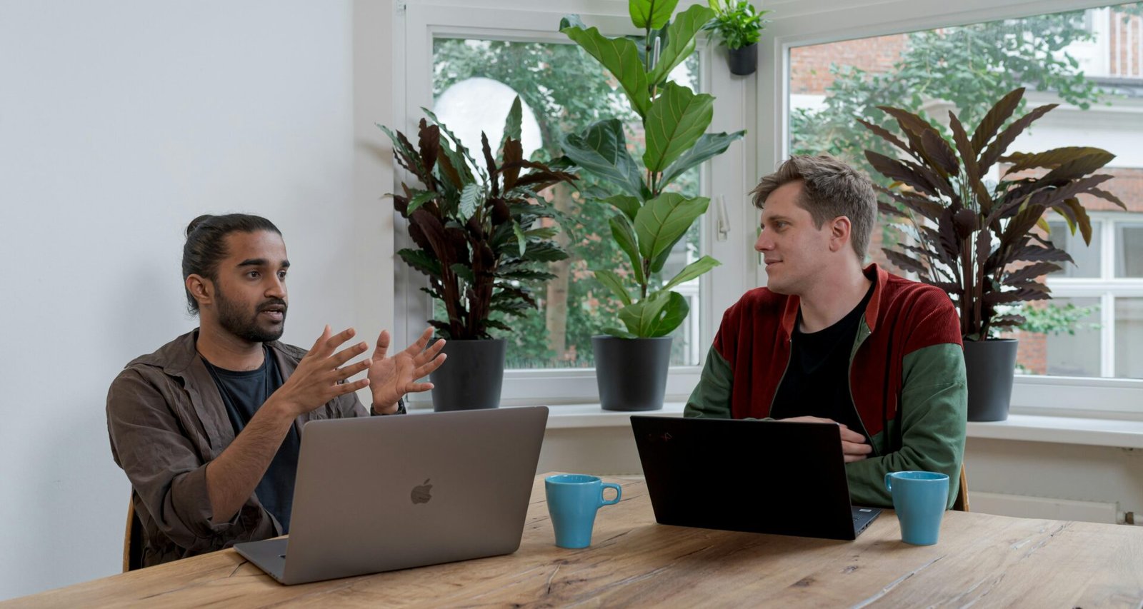 Mann im rot-schwarzen Shirt arbeitet konzentriert an einem silbernen MacBook an einem modernen Arbeitsplatz.