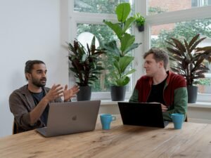 Mann im rot-schwarzen Shirt arbeitet konzentriert an einem silbernen MacBook an einem modernen Arbeitsplatz.