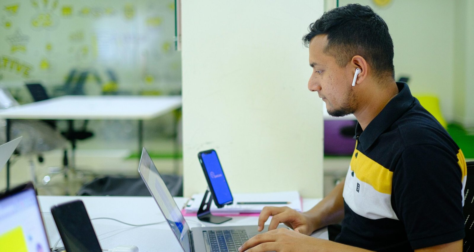 Mann im schwarzen und gelben Polohemd arbeitet im Büro an einem MacBook Pro an einem Schreibtisch mit modernen Arbeitsutensilien