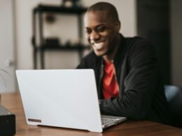 Ein Mann im schwarzen Blazer sitzt an einem Tisch und arbeitet mit einem Laptop in modernem Büroambiente.