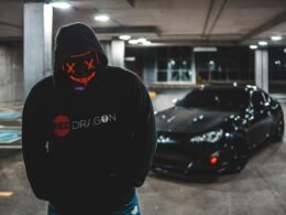 Mann in schwarzem Hoodie steht neben schwarzem Auto auf einer Straße, modernes und urbanes Setting im Fokus