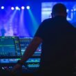 Ein Mann mit schwarzem T-Shirt bedient ein Audio-Mischpult in einem professionellen Tonstudio.