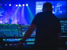 Ein Mann mit schwarzem T-Shirt bedient ein Audio-Mischpult in einem professionellen Tonstudio.